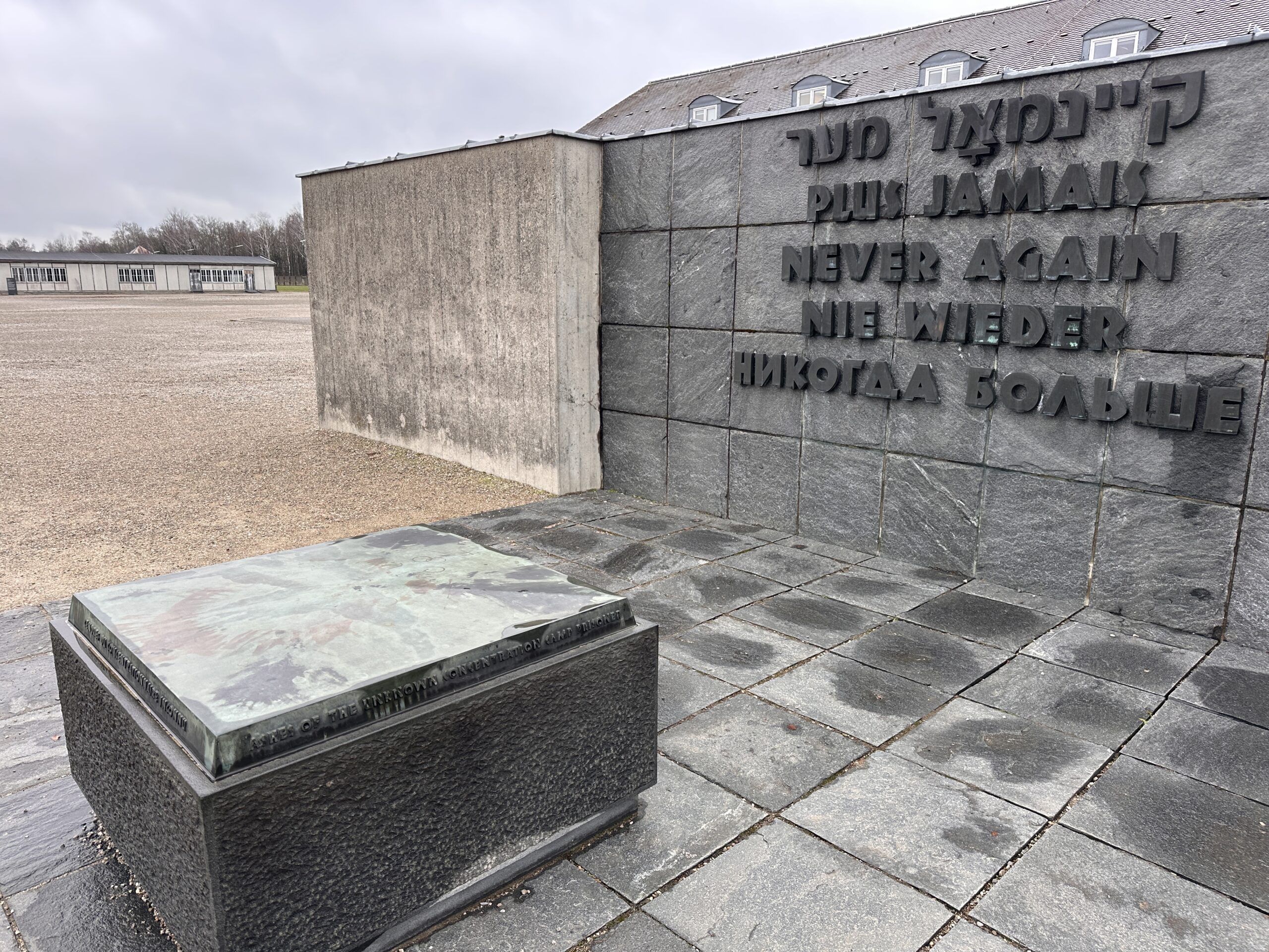 Stone monument at Dachau concentration camp with “Never Again” inscribed in five languages, honoring Holocaust victims and global remembrance.